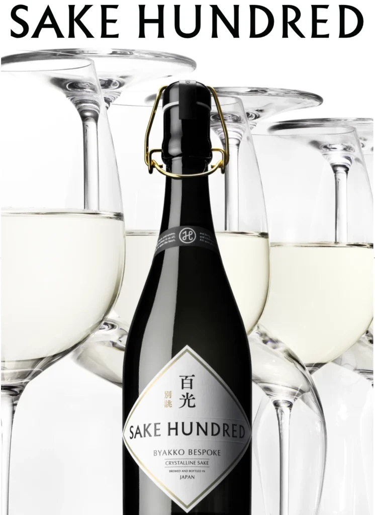 Black bottle labeled Sake Hundred Bespoke surrounded by large stemmed glasses filled with clear liquid
