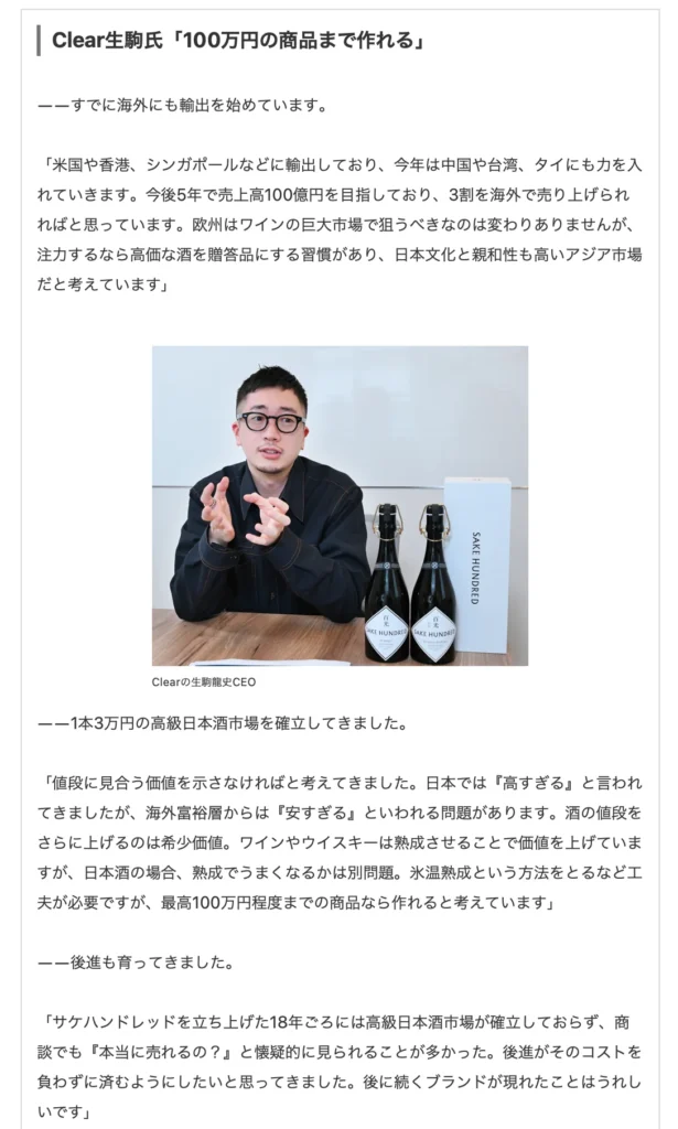 Man sitting at table with four bottles of sake and a dark blue box, gesturing with one hand