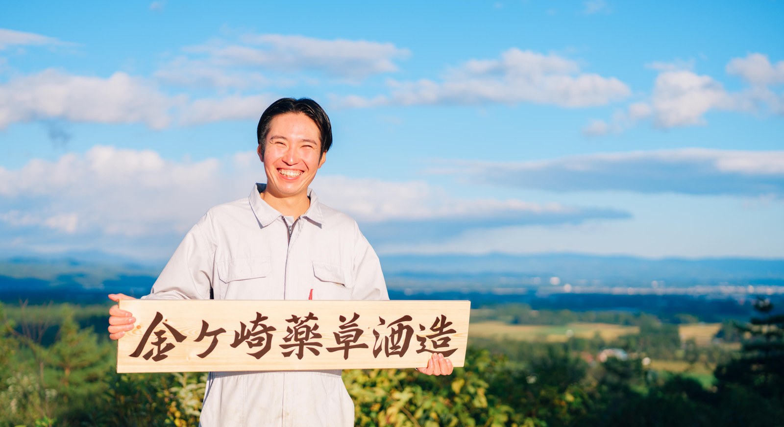 Kazuma Oikawa holding the Kanegasaki Herb Liqueur Distillery sign, Iwate